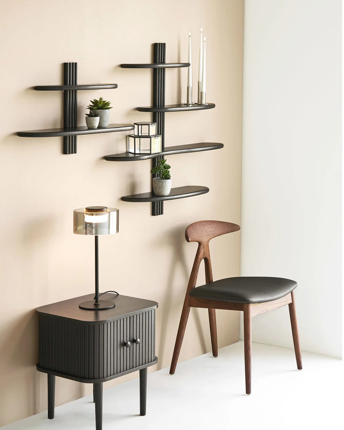 Sorte væghylder med to og tre hyldeplaner stylet med planter, lysestager og dekoration over et sort sengebord.