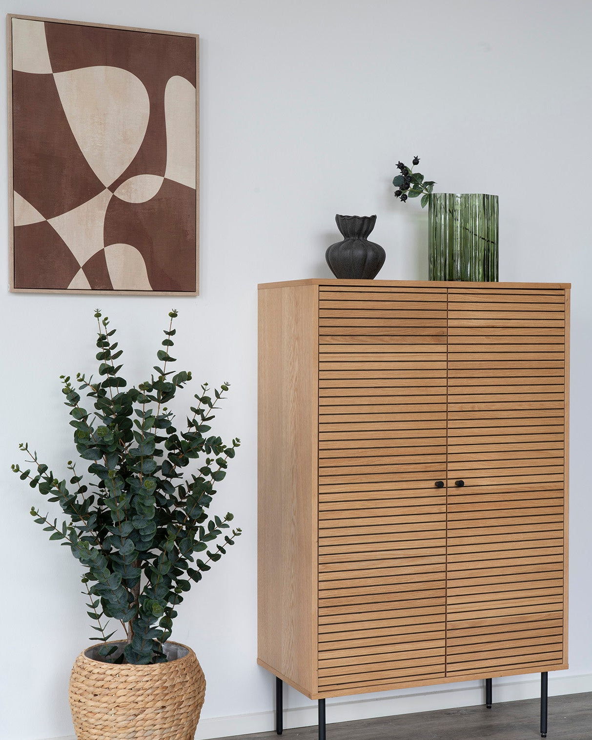 Grøn riflet glasvase stylet på egetræsskænk med abstrakt vægkunst og eucalyptus