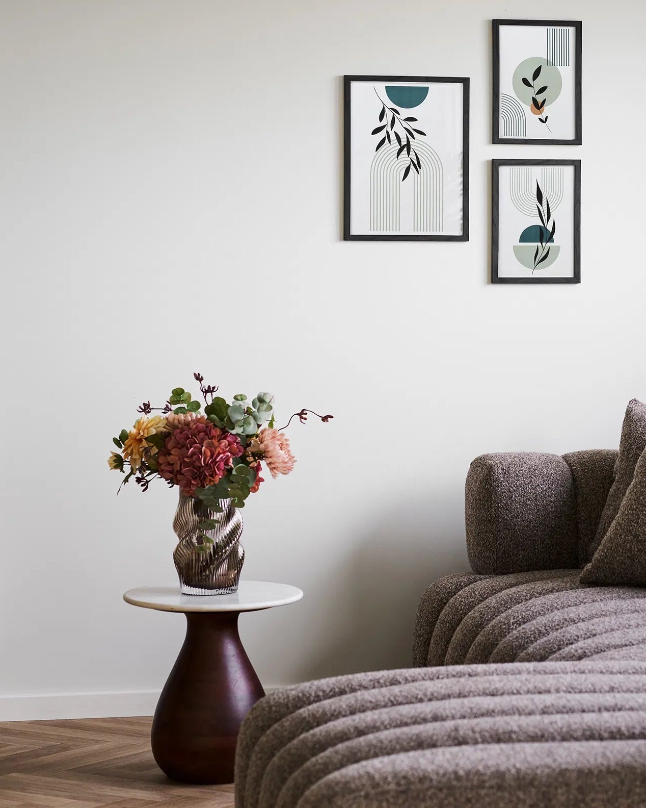 Mundblæst vase i brun med snoede organisk former og billeder på væggen i baggrunden.