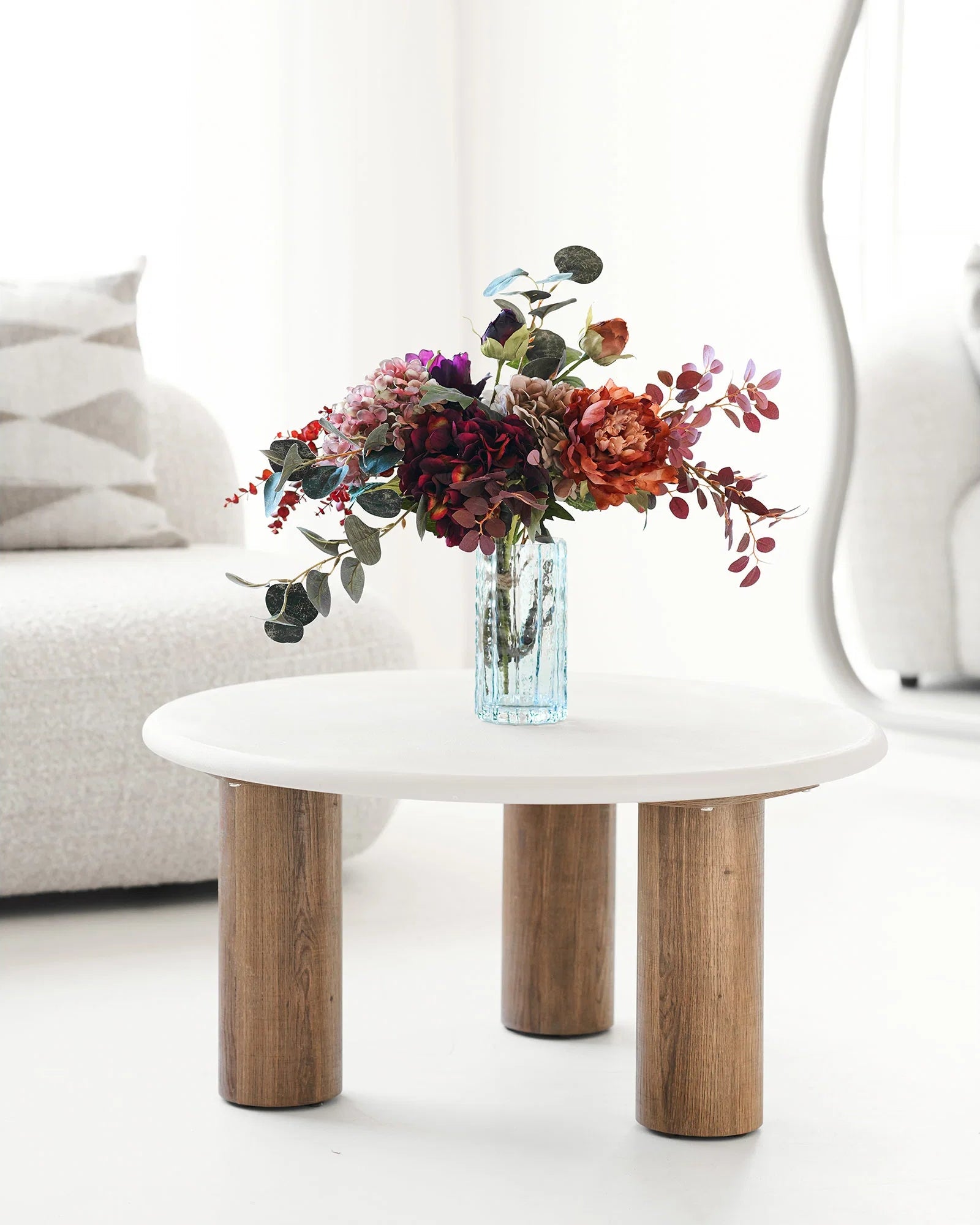 Klar struktureret glasvase med farverig blomsterbuket på rundt sofabord