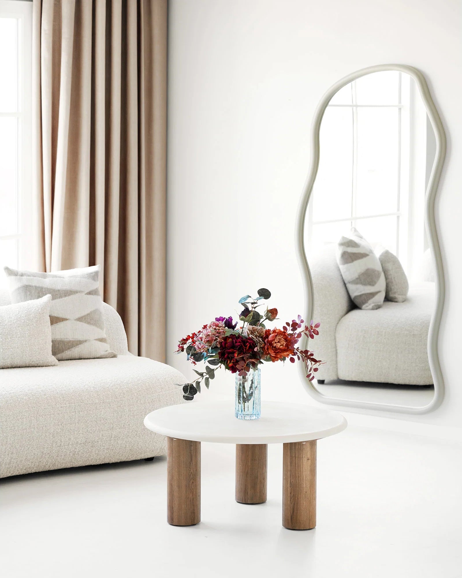Klar glasvase med farverig buket i lys stue med organisk spejl og beige sofa
