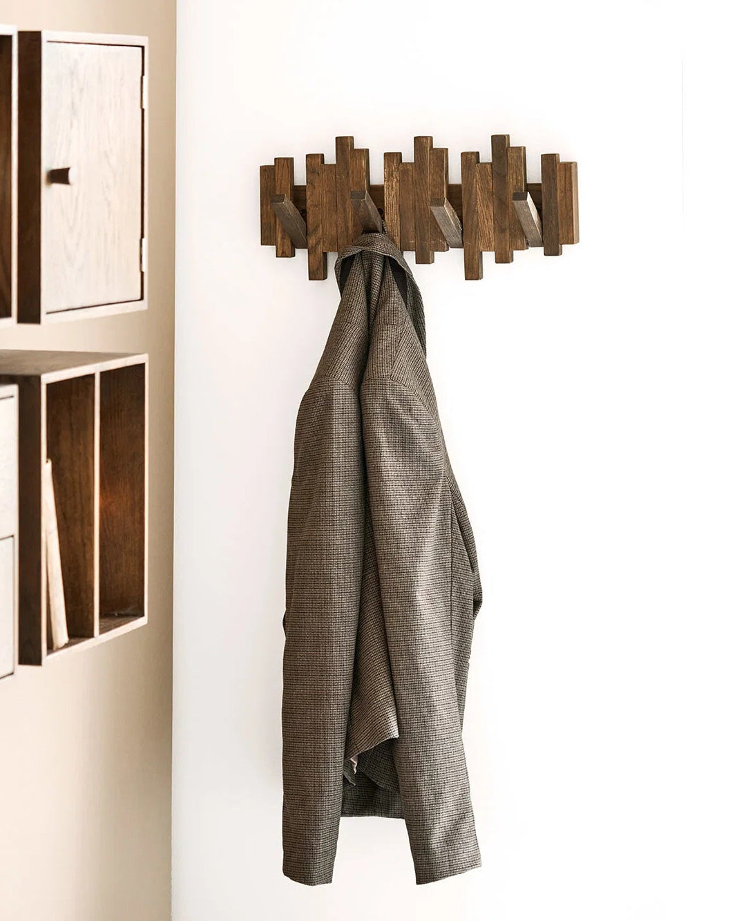 Mørkebrun knagerække i træ med geometrisk design stylet i entré med jakke hængende på knage.