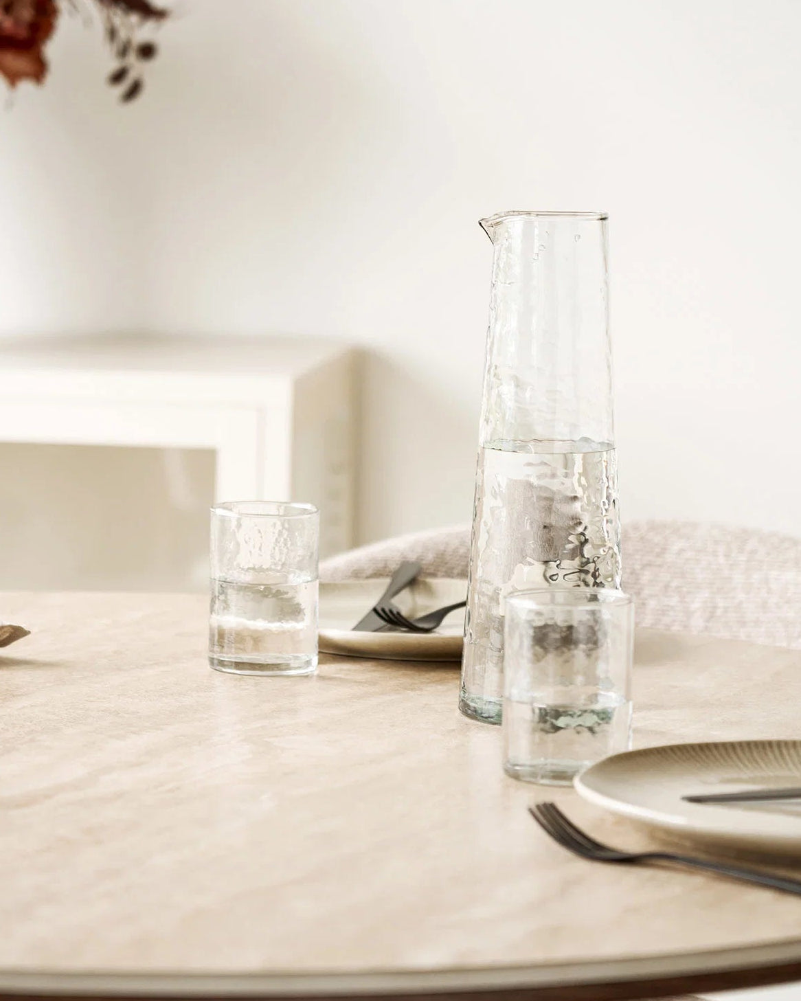 Klar glaskaraffel med vand og matchende drikkeglas på spisebord i nordisk indretning.