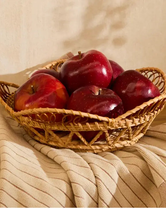 Håndflettet frugtkurv med røde æbler på beige tekstil i varm og naturlig indretning
