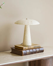 Beige bordlampe i travertin med svampeformet design stylet på konsolbord med bøger og blomster.