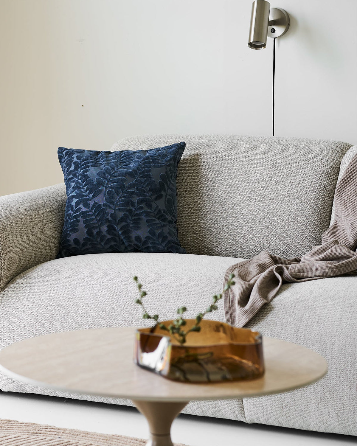 Skandinavisk stue med væglampe i børstet stål og beige sofa
