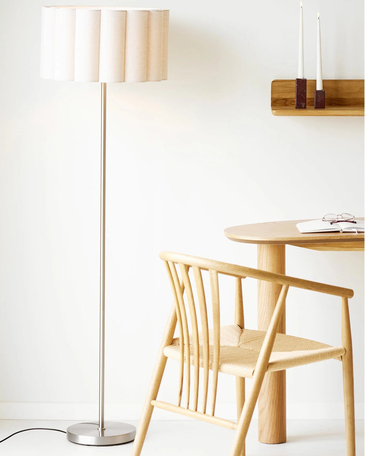 Gulvlampe med beige plisseret lampeskærm og slank fod i børstet stål stylet i lyst nordisk interiør.