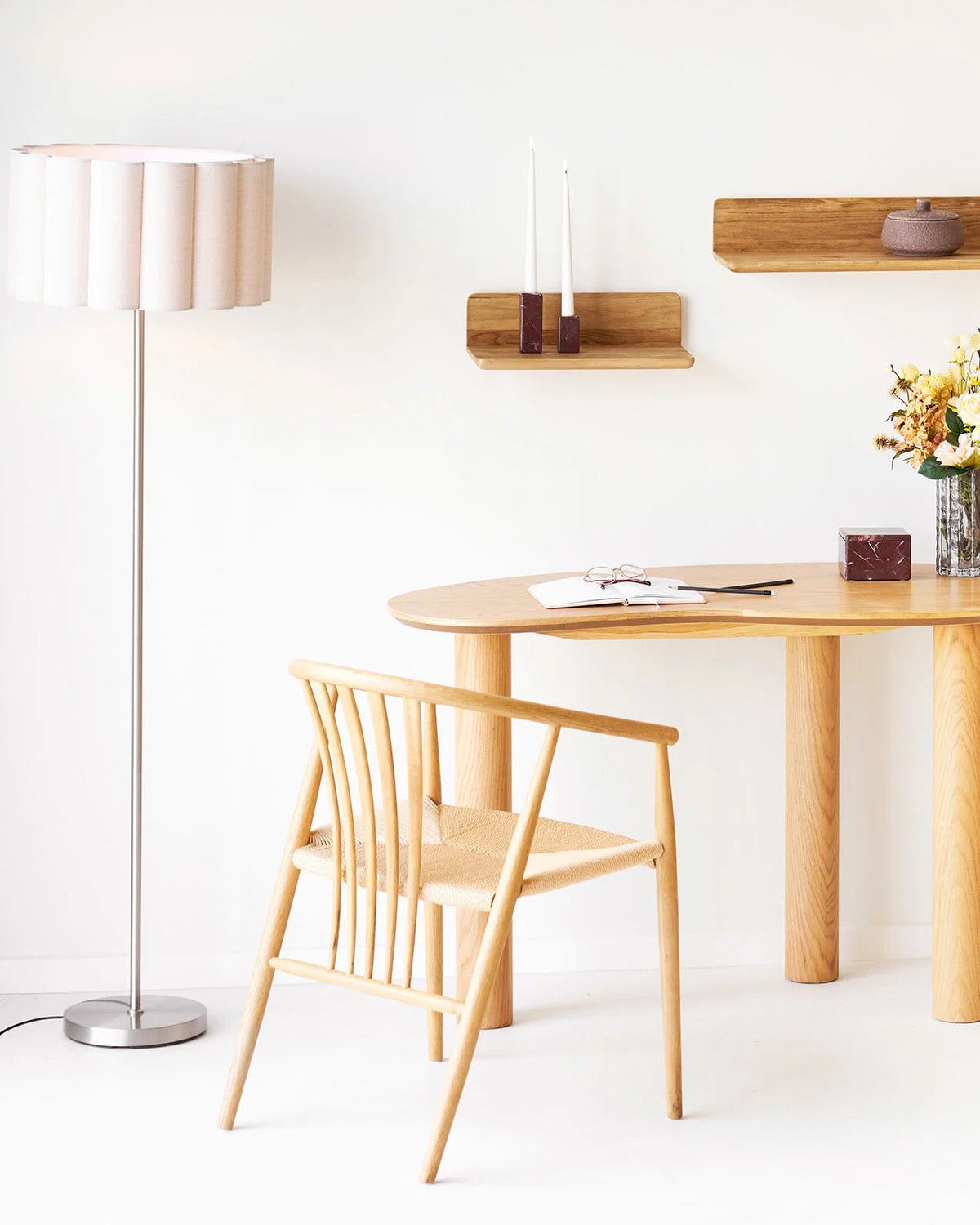 Gulvlampe med beige plisseret skærm stylet ved spisebord i lyst nordisk interiør med træmøbler.