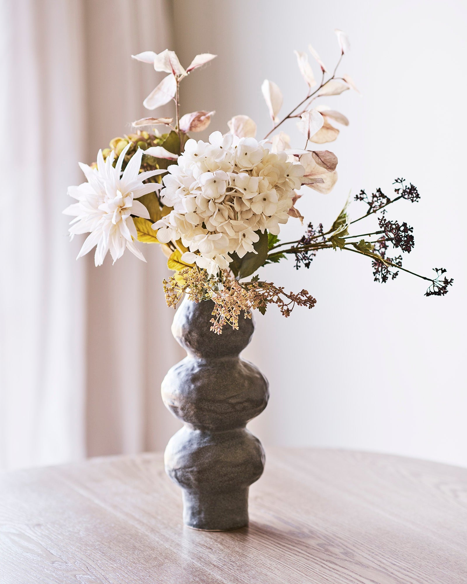 Kunstig blomsterbuket i vase med hvide hortensiaer og dahlia på spisebord
