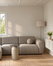 Gulvlampe med beige plisseret lampeskærm stylet ved lys sofa i hyggelig nordisk stue.