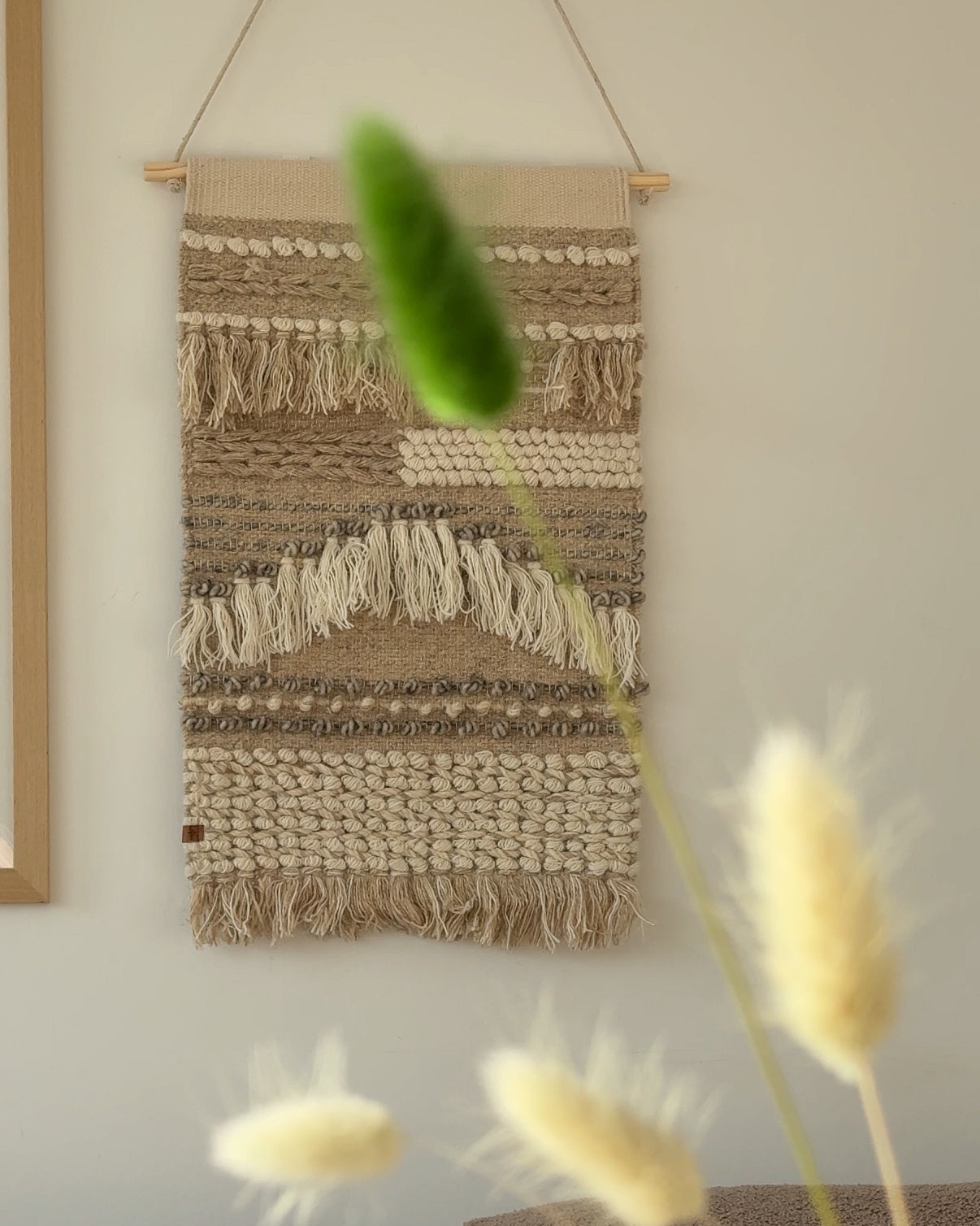 Vægtæppe i beige på hvid væg med blomster foran