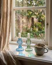 Pesce lysestagerne i blå og grøn i vindueskarm med gardiner og varm kaffe