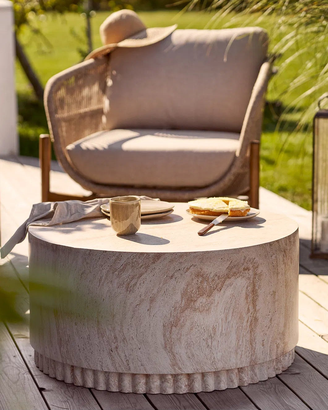 Kyst keramikkrus stående på et lavt, rundt sofabord i sten på en solrig terrasse, ved siden af en kage.