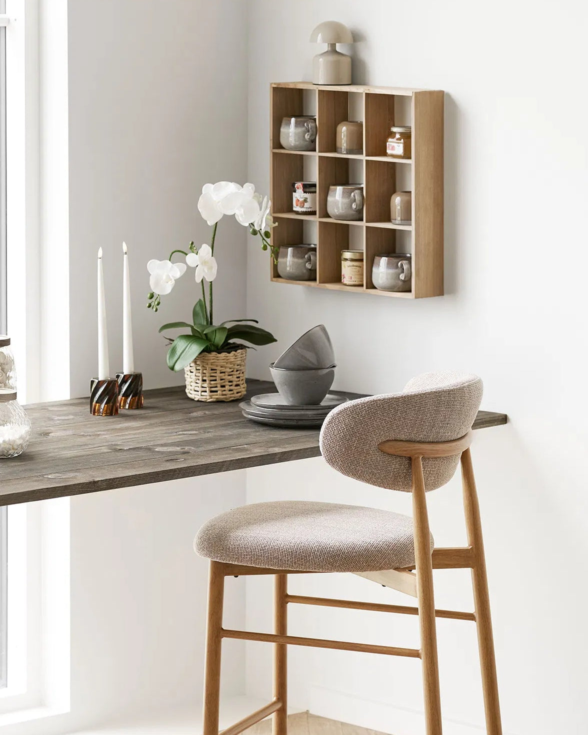 Rute væghylde stylet i en lys spisestue med et mørkt træbord, en polstret spisebordsstol og en hvid orkidé. Hylden bruges til udstilling af keramik
