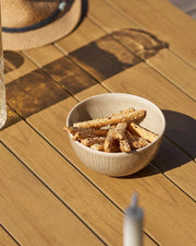 keramikskål fyldt med salte snacks, stående på et havebord i træ i solskinnet.