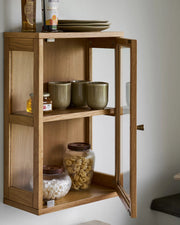 Nærbillede af Eik vitrineskabet i brug i køkkenet, fyldt med grønne keramikkopper, pasta i glas og delikatesser.