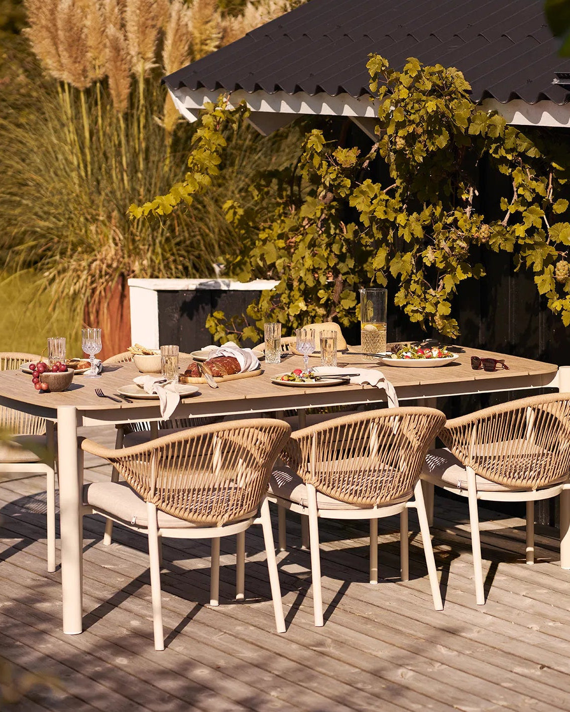 Smukt dækket havebord på en terrasse med Kyst middagstallerkener brugt til servering af salat og brød ved solnedgang.