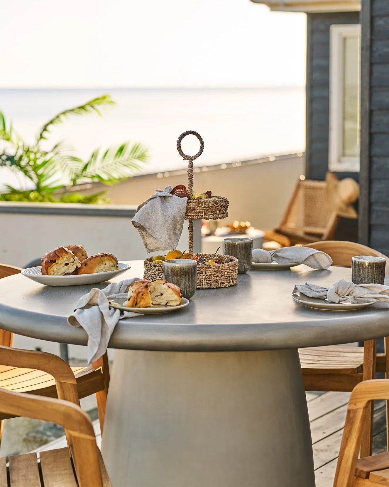 Smukt dækket rundt bord på en terrasse med havudsigt, hvor Kyst frokosttallerkener er brugt til servering af brød.