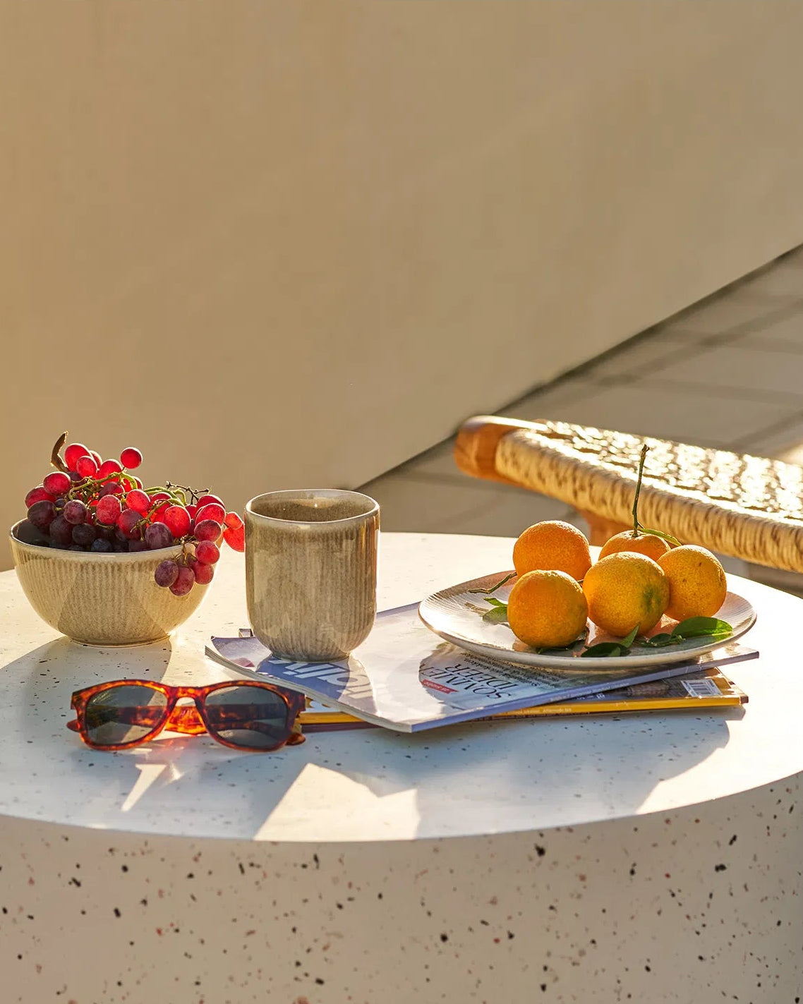 Kyst frokosttallerken fyldt med friske appelsiner, stylet på et lyst rundt bord på terrassen sammen med vindruer og solbriller.