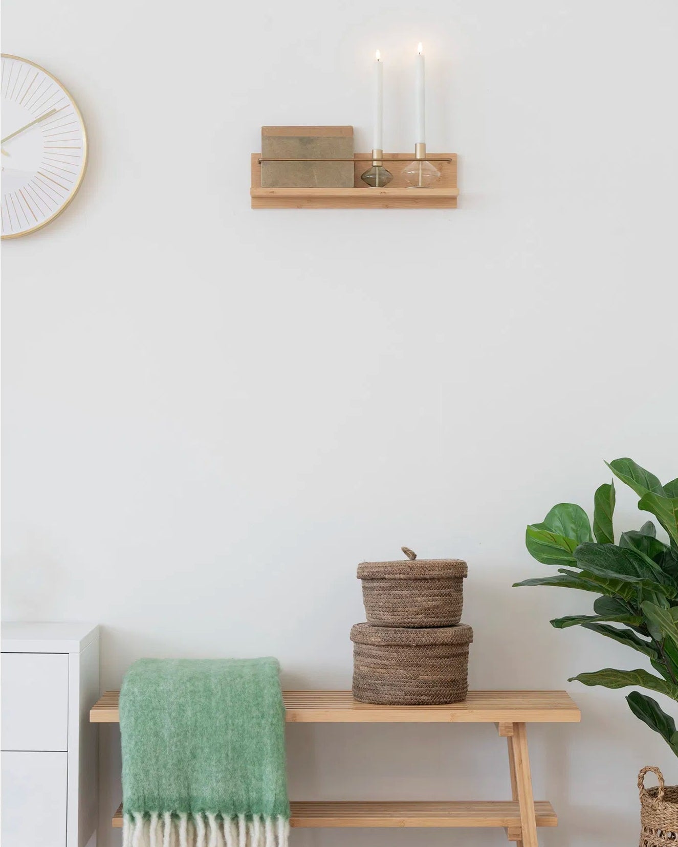 Palma væghylde i bambus stylet på en hvid væg med levende lys og dekorationer. Viser hylden i et hyggeligt, nordisk hjemmemiljø.