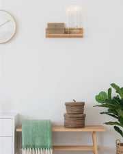 Palma væghylde i bambus stylet på en hvid væg med levende lys og dekorationer. Viser hylden i et hyggeligt, nordisk hjemmemiljø.