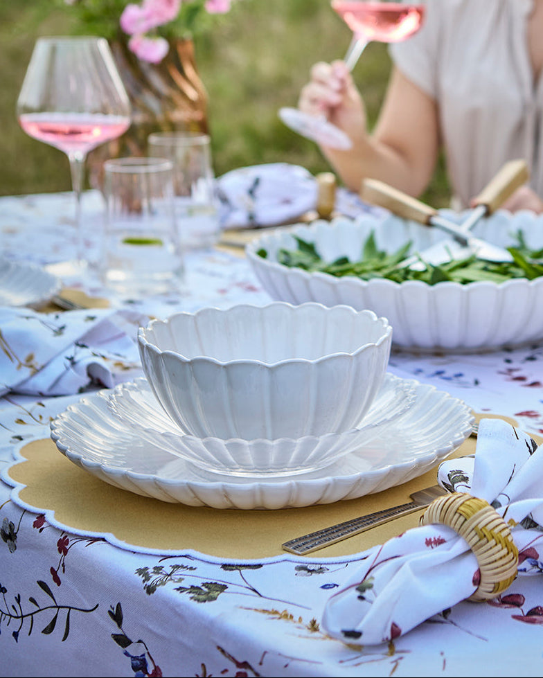 Flor middagstallerkenen i hvid sammen med flor skål i hvid på et sommerbord med mad og vin i baggrunden