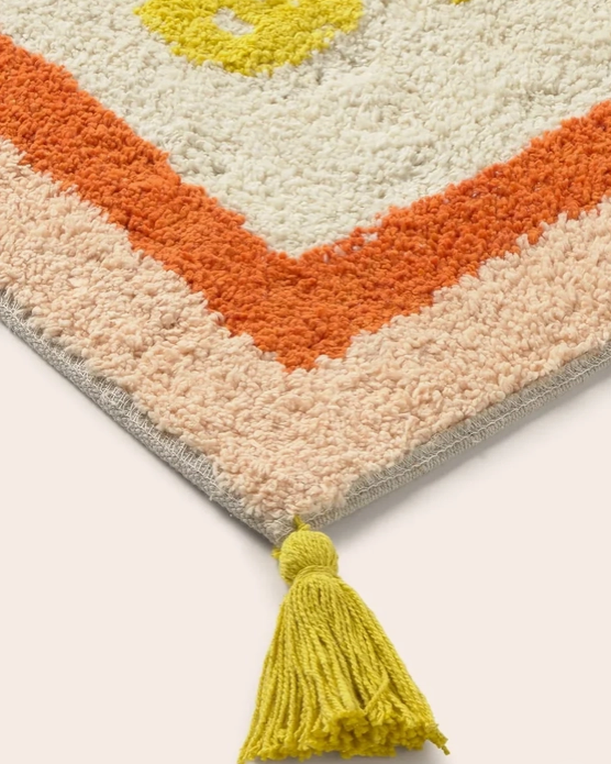Detaljebillede af badeværelsesmåtte med teksten "Bath Club" i varme farver
med pompom