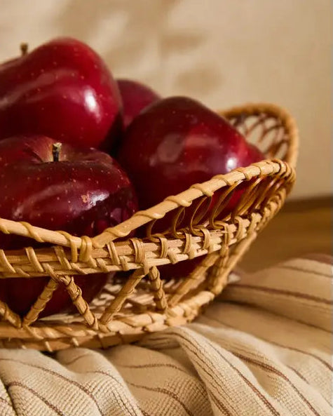 Håndflettet frugtkurv med røde æbler tæt på med beige tekstil i varm og naturlig indretning