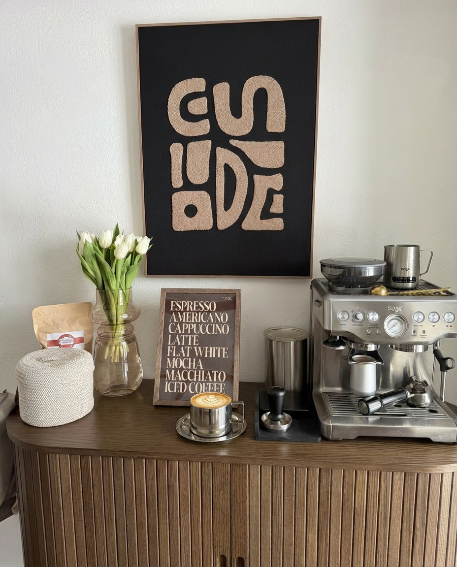Rustfrit stål kaffekop med underkop på træbord omgivet af kaffebønner og kaffeudstyr